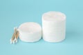 Two stacks of round cotton pads and heap of wood stick cotton buds on blue background. Hygiene supplies, beauty tools and skincare