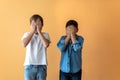 Two standing children covering their faces with their hands