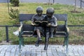 Two statuettes, standing reading on a park bench