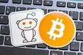 Two stickers, one of the Reddit logo mascot and the other of the Bitcoin symbol, on a laptop computer keyboard, social media and Royalty Free Stock Photo