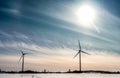 Two stopped windmills, no wind. Frozen coast of Baltic Sea. Big Sun at sky with blue rose cirrus light clouds. Cold Sunny day at Royalty Free Stock Photo