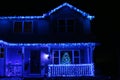 A two story house decorated with blue Christmas lights on the roofline and front porch with a lit Christmas tree in the window Royalty Free Stock Photo