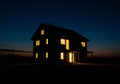 A two-story house with illuminated windows stands against a twilight sky. The structure Royalty Free Stock Photo