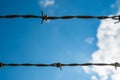Two strands of barbed wire with blue sky and clouds in the background Royalty Free Stock Photo