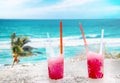 Two strawberry red drift-ice with straw on the beach. Two apple green drift-ice with straw on the beach. In the background is blue