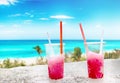 Two strawberry red drift-ice with straw on the beach. In the background is blue sky, palms, sea nd sandy beach. This is situated