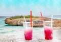 Two strawberry red drift-ice with straw on the beach. In the background is blue sky, sea nd sandy beach. This is situated in