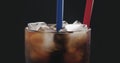 Two straws in cola with ice cubes in glass over black background