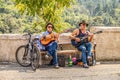 Two street musicians sit on bench at tourist spot near castle above city playing guitars with beer Royalty Free Stock Photo