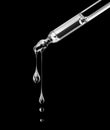 Two stretched oily drops falls from a pipette close-up on a black background