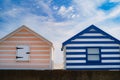 Two striped wooden beach huts on a day with blue sky and white clouds