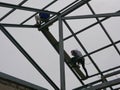 Two structural steel workers working on a high rooftop for a house roof structure installation