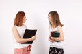 Two student over a white wall, one is holding books in hands and other a clipboard Royalty Free Stock Photo