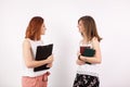 Two student over a white wall, one is holding books in hands and other a clipboard Royalty Free Stock Photo