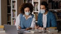 Two students in medical masks sit at desk in university library listen to teacher in headphones on laptop study write Royalty Free Stock Photo