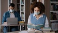 Two students in medical masks studying preparing for exam in university library young guy working typing on laptop girl Royalty Free Stock Photo