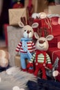 Two stylish amigurumi deers in striped sweaters, scarf and butterfly tie stands near Christmas presents