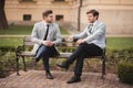 Two stylish businessmen speaking and smiling outdoors