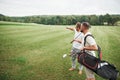 Two stylish men holding bags with clubs and walking on golf course Royalty Free Stock Photo
