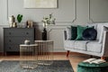 Two stylish small coffee tables with marble tops in front of elegant grey couch with emerald pillows