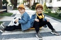 Two stylish twin boys sitting on the skateboard or pennyboard looking each over up in the street.