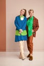 Two stylish women in bright colorful clothes standing in studio. Fashion female models wear elegant suits