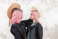 Two stylish young women with beautiful pink hair in trendy youth jackets look at each other and take off their hats. Attractive Royalty Free Stock Photo