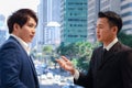 Two successful businessmen in suit talking and discussing at modern city downtown with skyscraper building as blurred background, Royalty Free Stock Photo