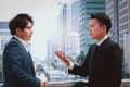 Two successful businessmen in suit talking and discussing at modern city downtown with skyscraper building as blurred background, Royalty Free Stock Photo