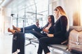 Two successful women resting in arrival hall waiting for a transfer sitting with their legs on suitcase surfing the Royalty Free Stock Photo