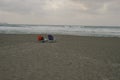 Two sun loungers on a large sandy beach next to a rough sea in cloudy weather