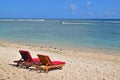 Two sundecks with red cushions on sandy beach facing clean azure blue sea with speed boat in background