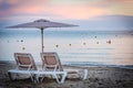 Two sun lounges and umbrella on the beach with pink sunset in the background Royalty Free Stock Photo