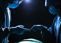 Two surgeons working and passing surgical equipment in the operating room, dark Royalty Free Stock Photo