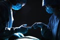 Two surgeons working and passing surgical equipment in the operating room, dark