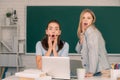 Two surprised students girls friends in classroom at school college or university on blackboard background. Learning and Royalty Free Stock Photo