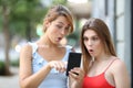 Two surprised women checking news on smartphone