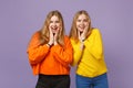 Two surprised young blonde twins sisters girls in vivid colorful clothes putting hands on cheeks isolated on pastel Royalty Free Stock Photo