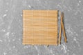 Two sushi chopsticks with empty brown bamboo mat or wood plate on cement Background Top view with copy space. empty asian food Royalty Free Stock Photo