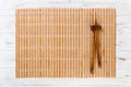 Two sushi chopsticks with empty brown bamboo mat or wood plate on white wooden Background Top view with copy space. empty asian Royalty Free Stock Photo