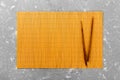 Two sushi chopsticks with empty yellow bamboo mat or wood plate on cement Background Top view with copy space. empty asian food Royalty Free Stock Photo