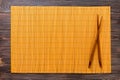 Two sushi chopsticks with yellow empty bamboo mat or wood plate on wooden Background Top view with copy space. empty asian food Royalty Free Stock Photo