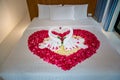 Two swans made from towels are kissing on honeymoon white bed.