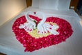 two swans made from towels are kissing on honeymoon white bed.
