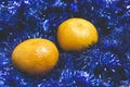 Two sweet, juicy mandarin lie on blue Christmas tinsel. Royalty Free Stock Photo