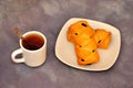 Two sweet puff buns with poppy seeds on a plate, next to a white porcelain cup of black tea on a gray background Royalty Free Stock Photo