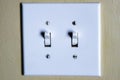 Two switch toggle light switch with white plastic cover on beige textured wall - lights turned on Royalty Free Stock Photo