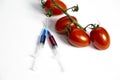 Two syringes with chemicals near a branch of tomatoes