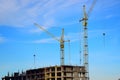 Two tall crane stand near a house under construction on blue sky background. Royalty Free Stock Photo