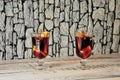 Two tall glasses with hot wine, fruit slices and spices stand on a wooden table against a stone wall Royalty Free Stock Photo